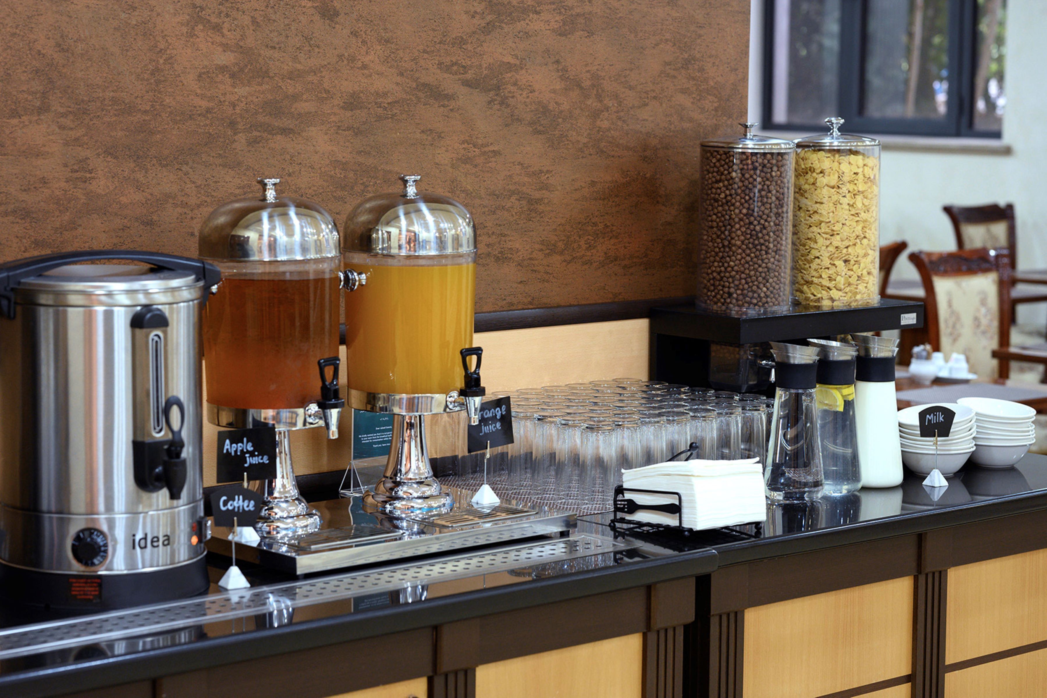 A coffee station with a coffee maker, two dispensers for orange juice and milk, and a stack of plates.