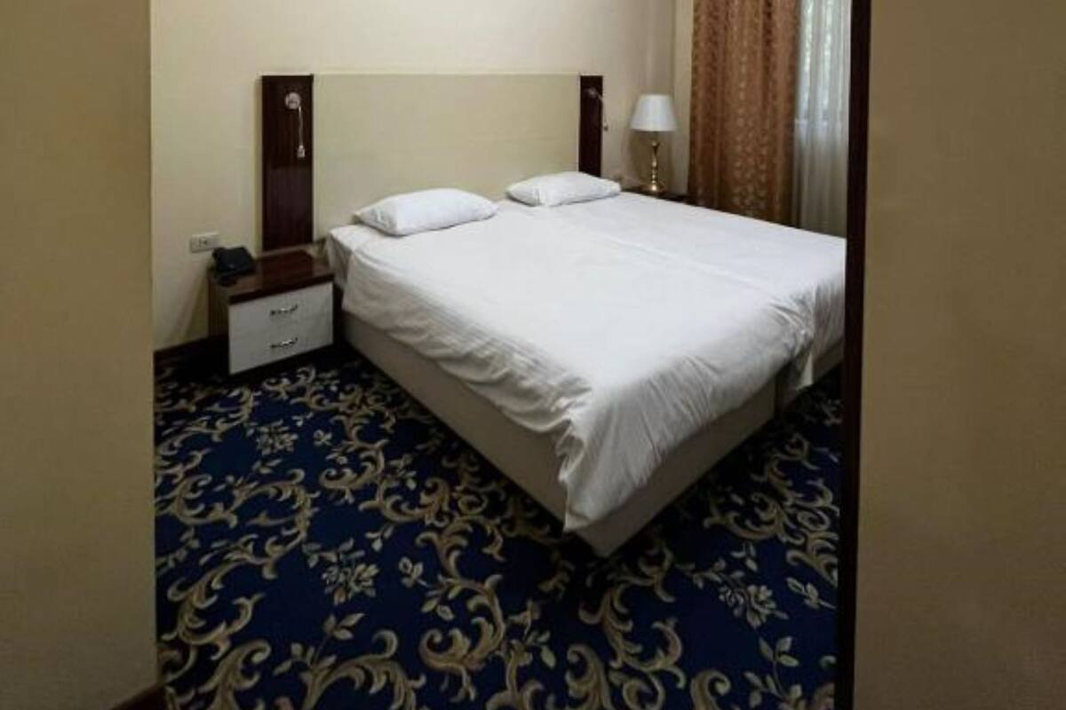 A hotel room with a large bed, a bedside table, a lamp, and a patterned carpet.