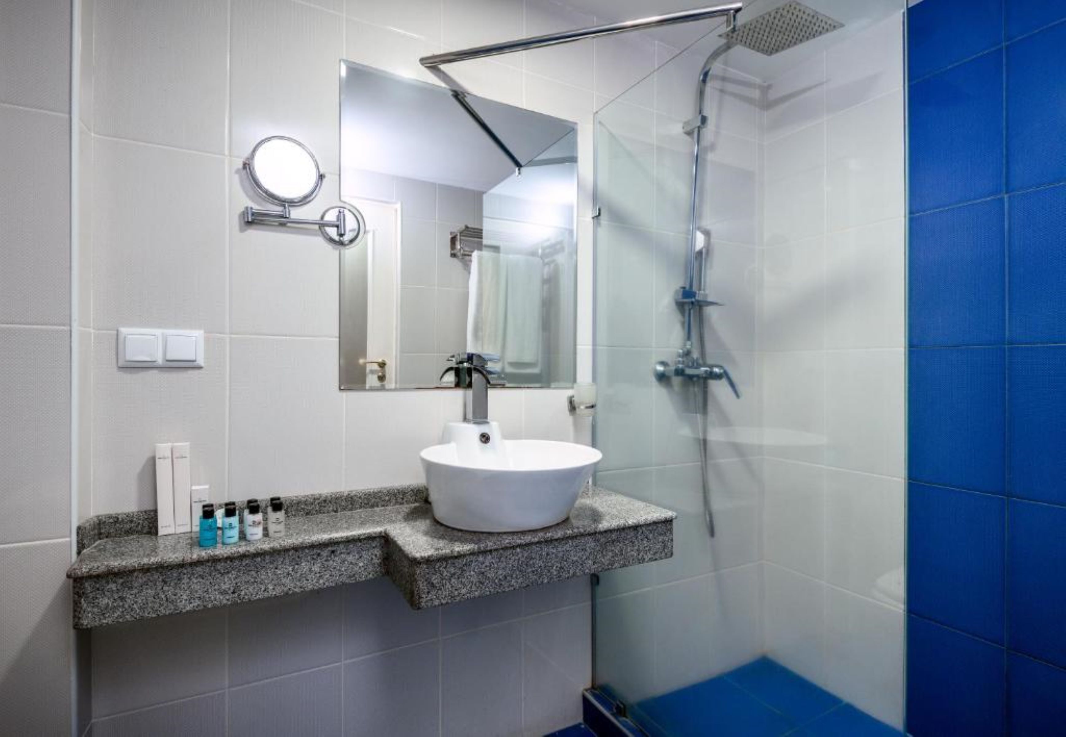 A modern bathroom with a granite countertop, a white sink, a handheld showerhead, and a mirror.