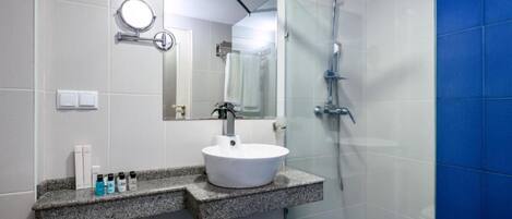 A modern bathroom with a granite countertop, a white sink, a handheld showerhead, and a mirror.