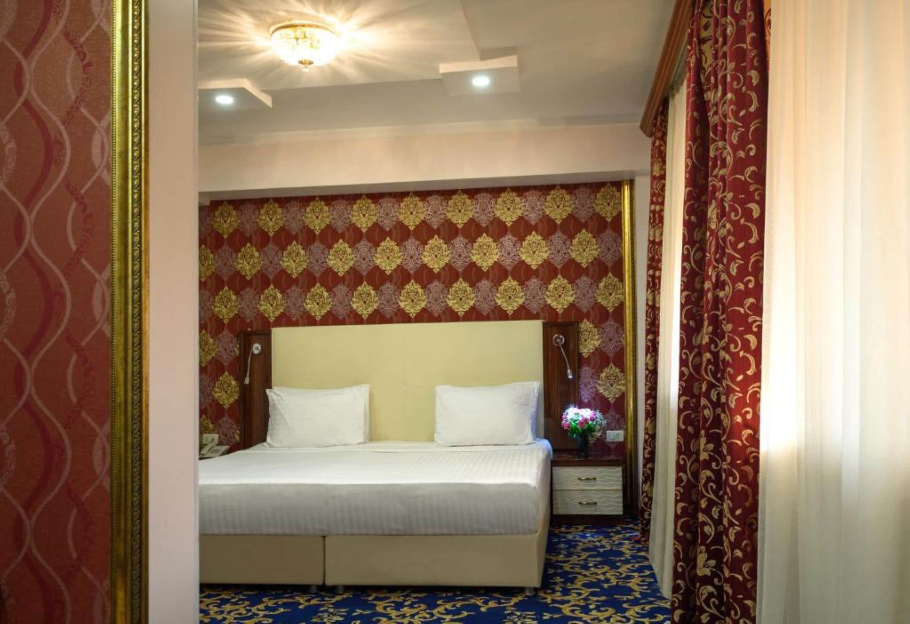 A hotel room with a large bed, a nightstand, and a wall with patterned wallpaper.