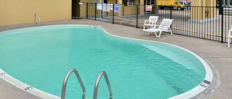 Une piscine à bord incurvé, une échelle en métal et des chaises longues blanches.