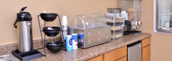 A kitchenette with a coffee maker, a rice cooker, a microwave, a toaster, and a coffee dispenser.