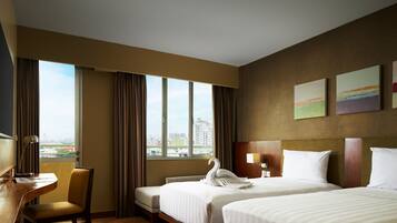 A hotel room with two beds, a desk, a chair, and a large window offering a city view.