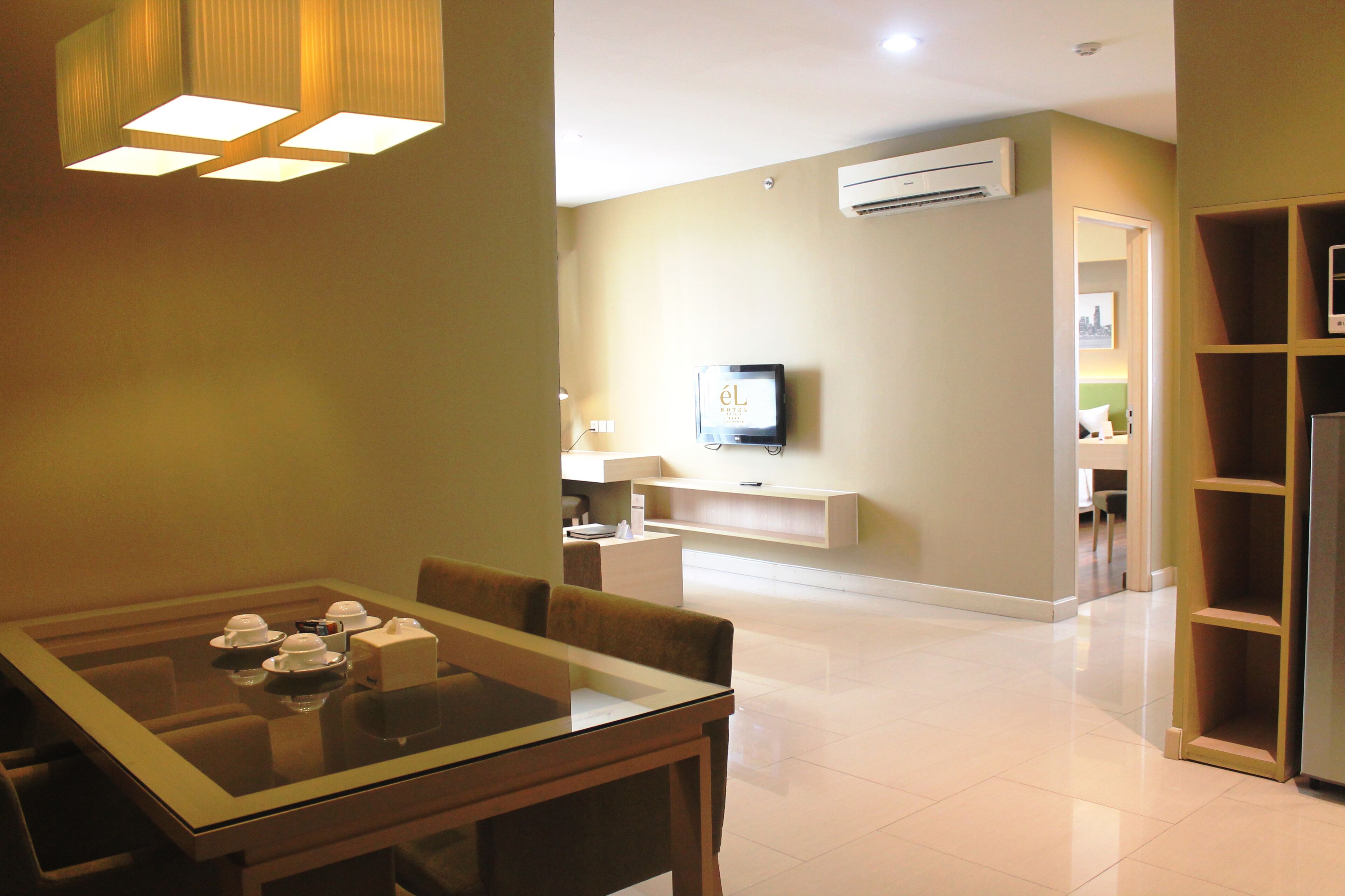 A hotel room with a dining area, a TV mounted on the wall, and a built-in bookshelf.
