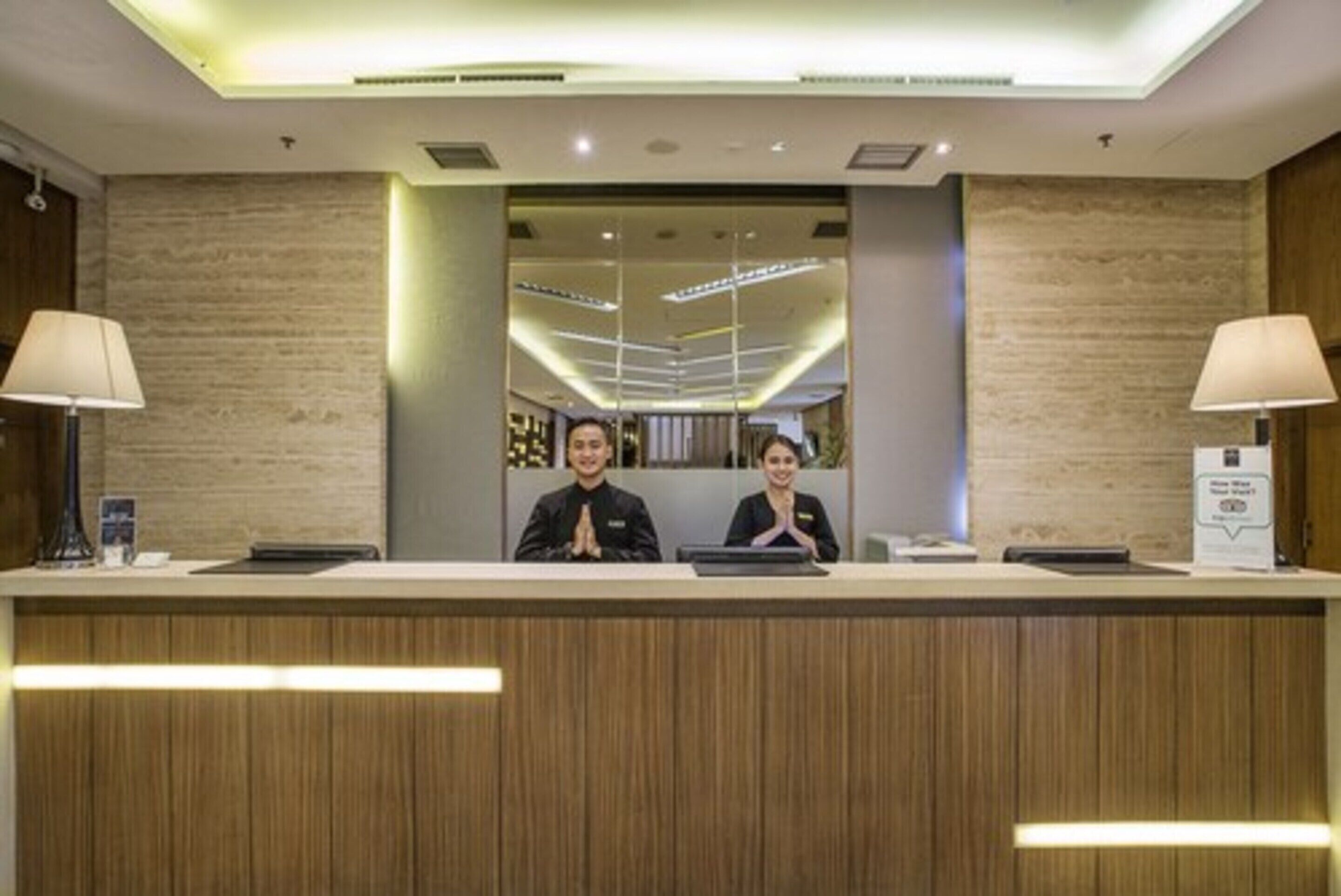 A reception desk with two staff members, a wooden panel design, and a modern interior.