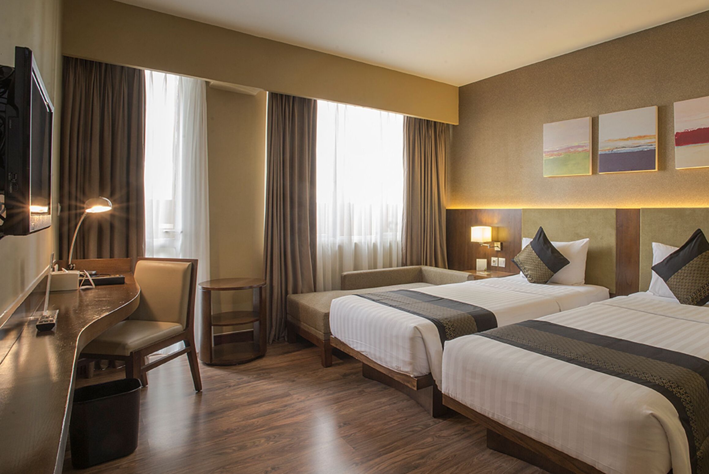 A hotel room with two beds, a desk, a chair, a TV, and a window with curtains.