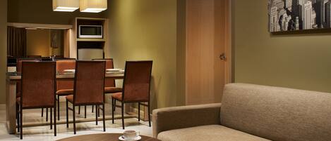 A hotel room with a dining area, a sofa, a coffee table, and a television.