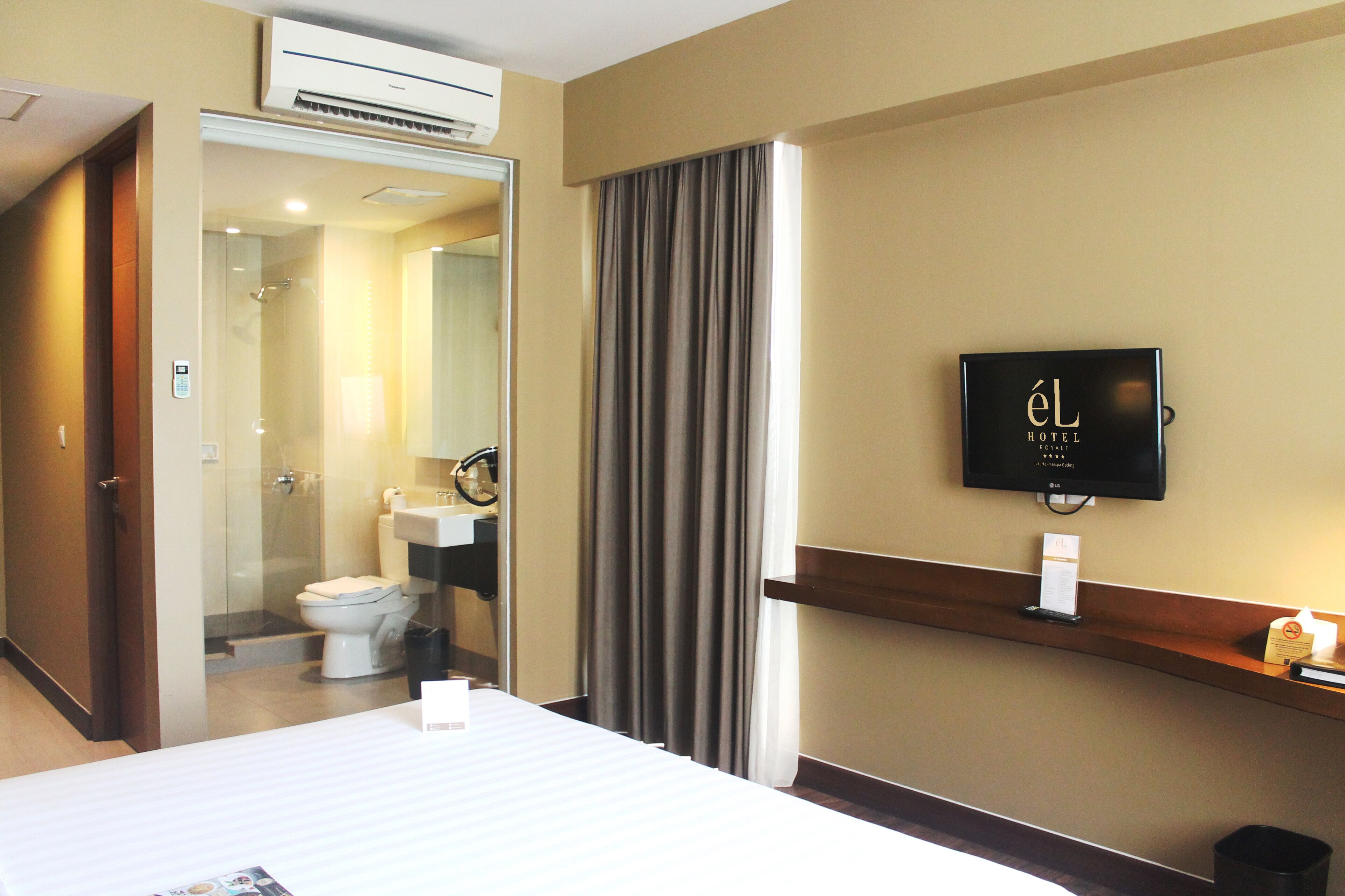 Une chambre d’hôtel comprenant un lit, un téléviseur fixé au mur, une salle de bain avec des toilettes et un lavabo, ainsi qu’une douche.