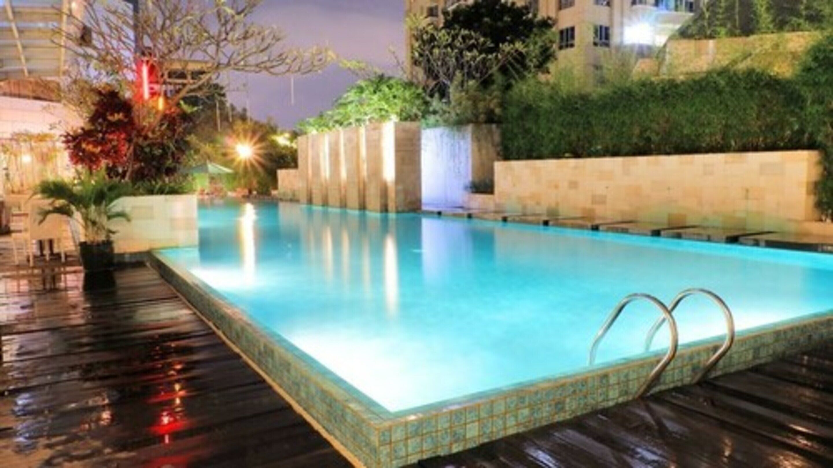 A rectangular swimming pool with a tiled edge, surrounded by a wooden deck and a low stone wall.