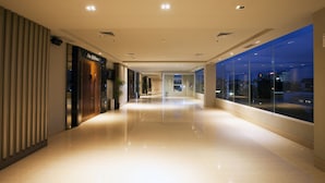 A modern hotel corridor with a reflective floor, a visible bathroom sign, and a large window offering a city view.