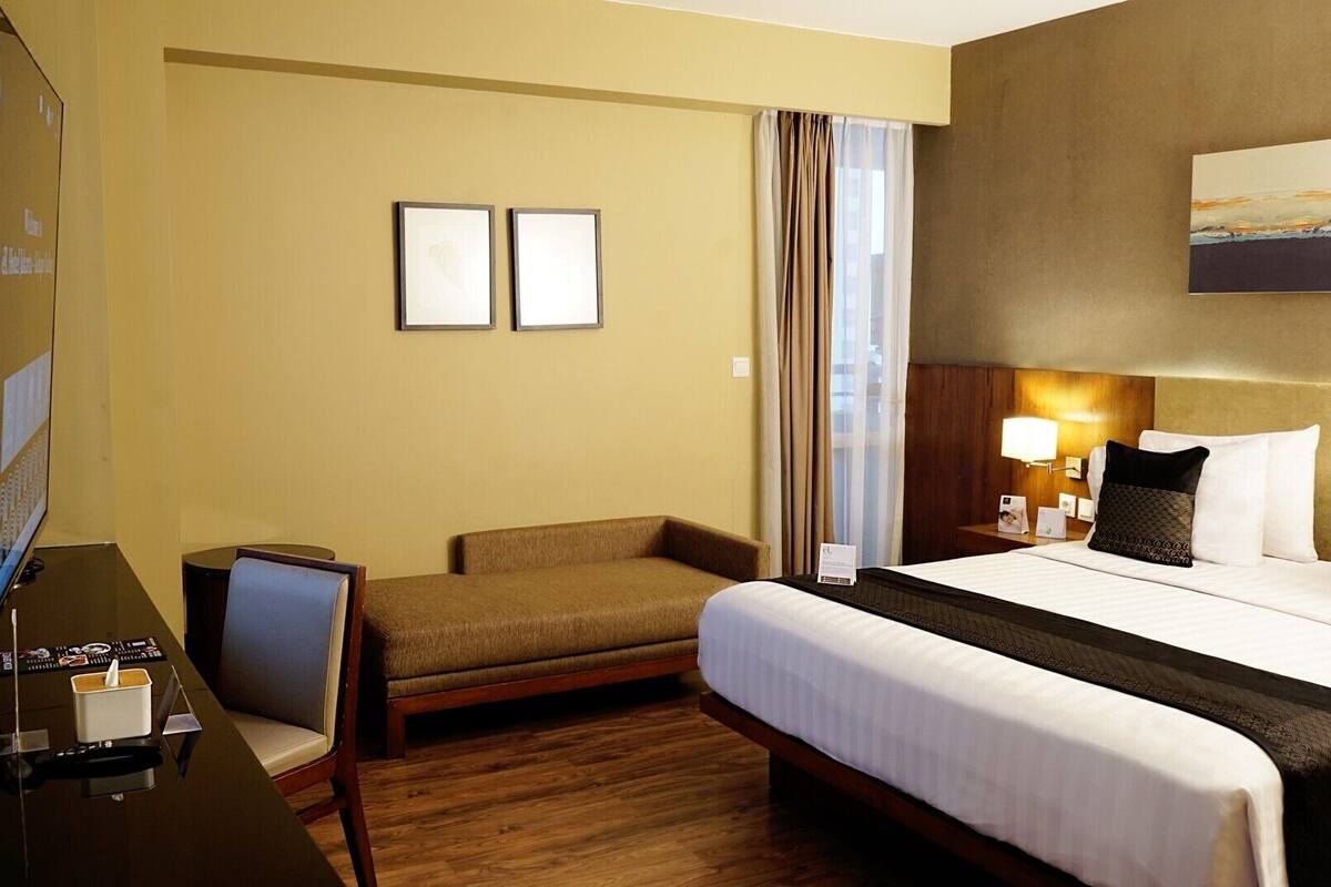 Ein Hotelzimmer mit Bett, Schreibtisch, Sessel, Fernseher und einem Bild an der Wand.
