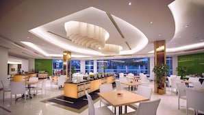 A modern hotel lobby with a central bar area, multiple seating arrangements, and large windows offering views of the cityscape.