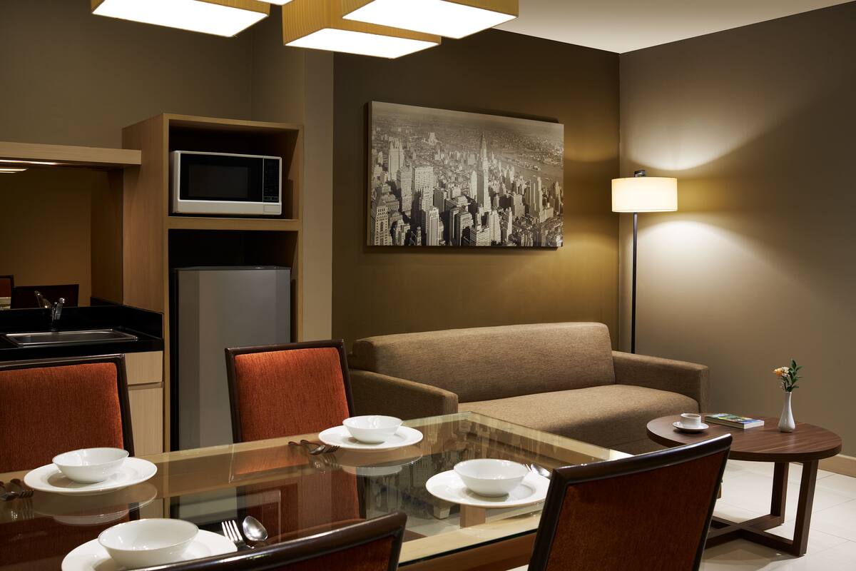 Ein modernes Hotelzimmer mit Essbereich, einer Couch, einer Mikrowelle und einem Bild an der Wand.