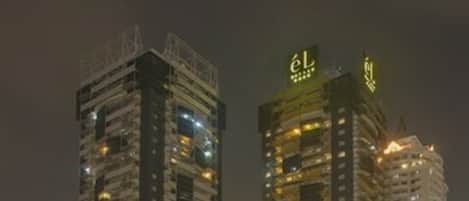 Two high-rise buildings with illuminated signage, surrounded by a parking area with motorcycles.