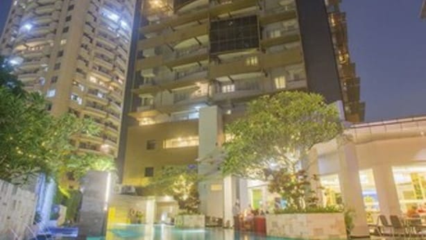 A high-rise building with multiple balconies, a swimming pool, and surrounding greenery.