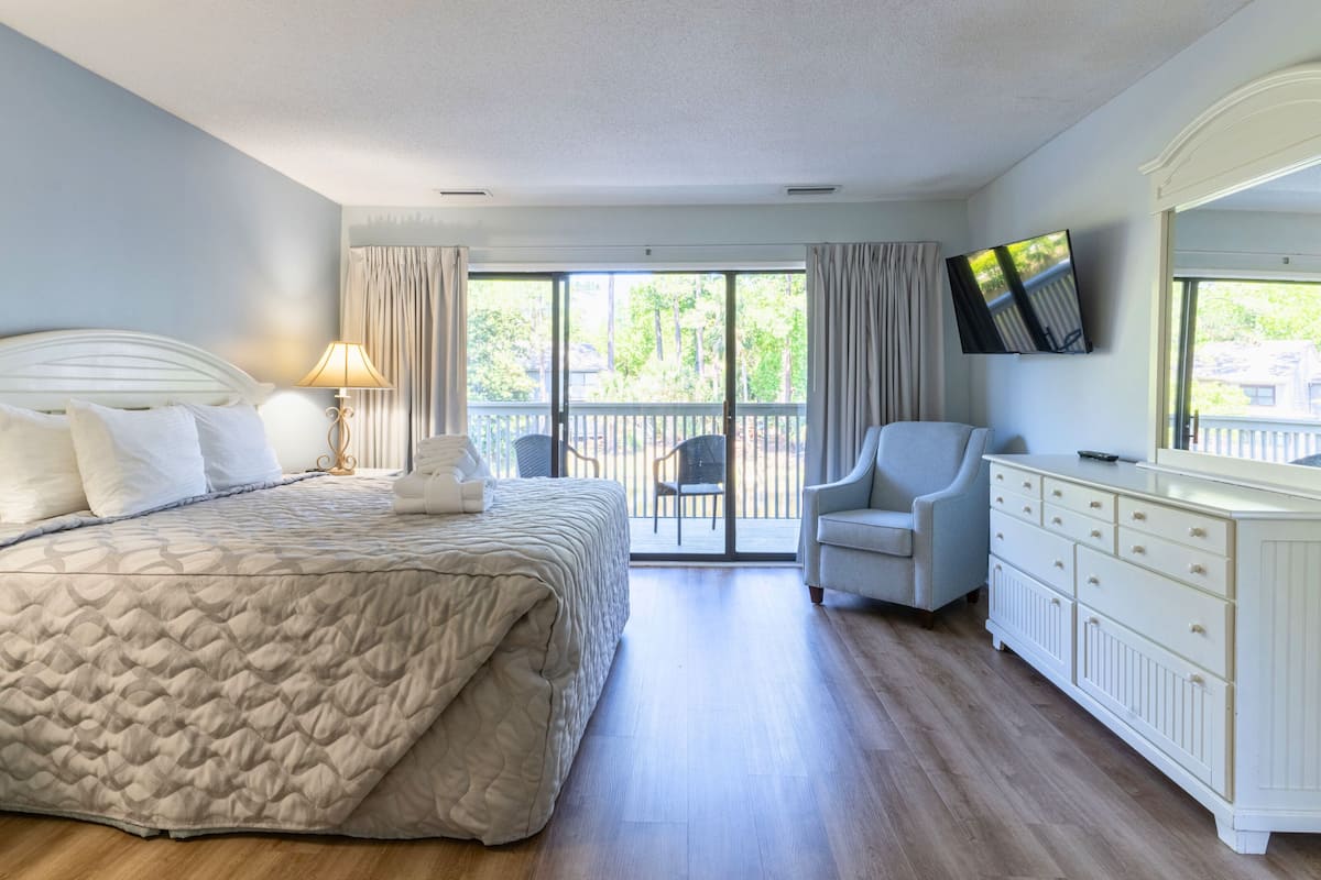 A hotel room with a bed, a chair, a TV, and a dresser.