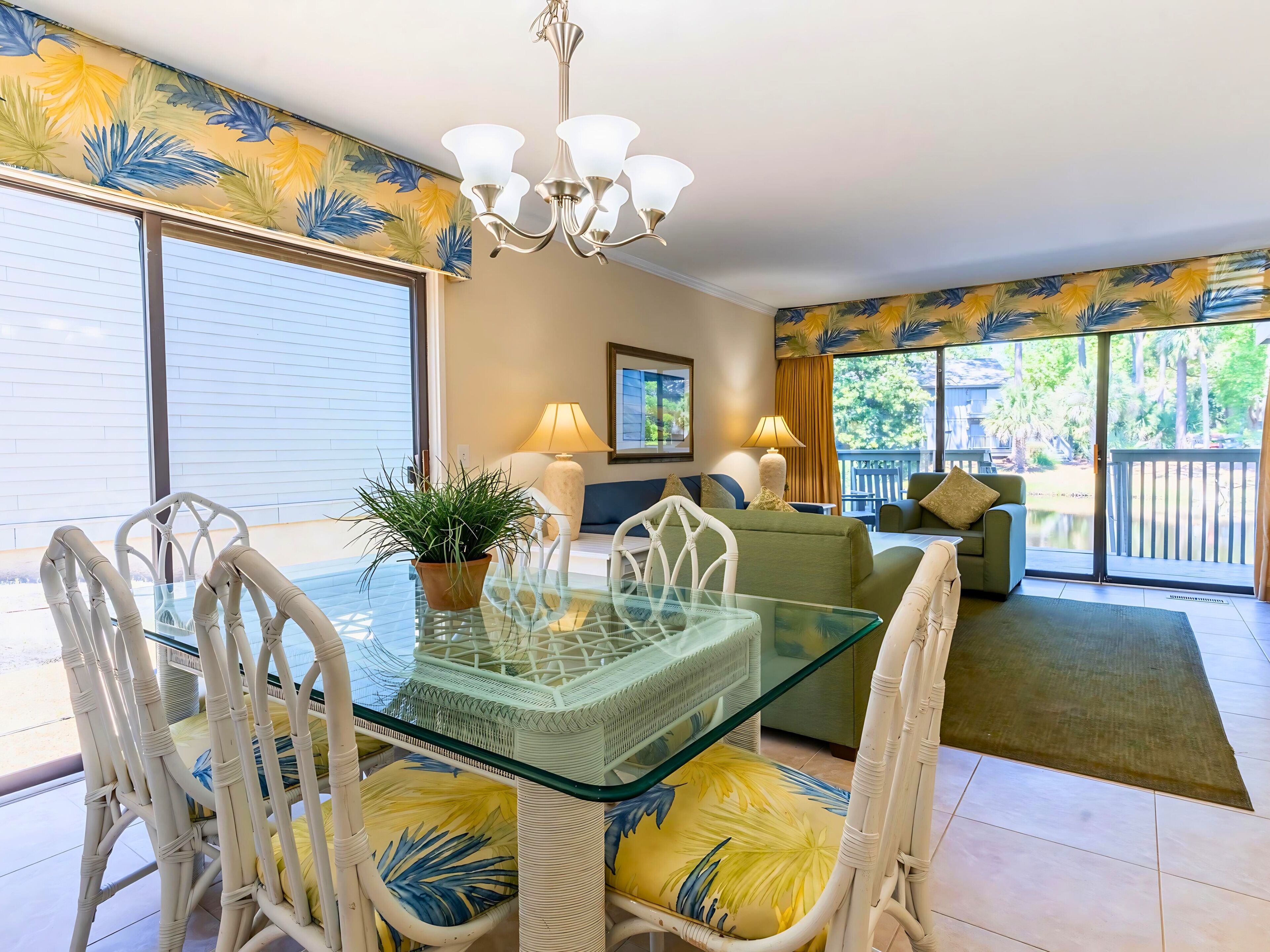 A spacious living area with a glass dining table, white wicker chairs, and a green sofa.