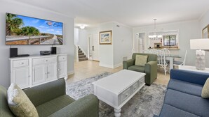 A spacious living area with a flat-screen TV, a dining table, and a staircase leading to another level. - Ocean Cove At Palmetto Dunes (Hilton Head Island)