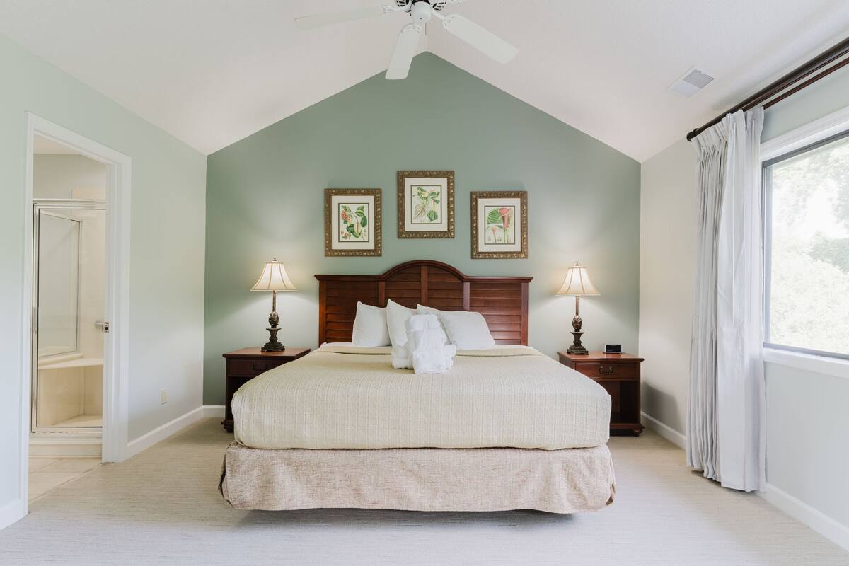 A bedroom with a large bed, two bedside tables with lamps, a ceiling fan, and framed artwork on the wall.