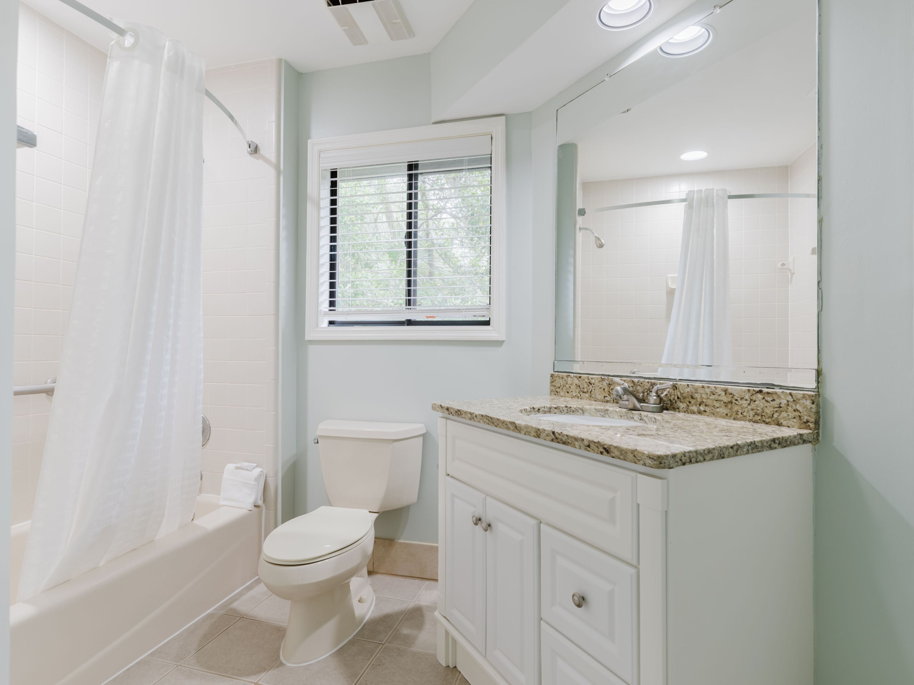 A bathroom with a bathtub, toilet, sink, and window with blinds.