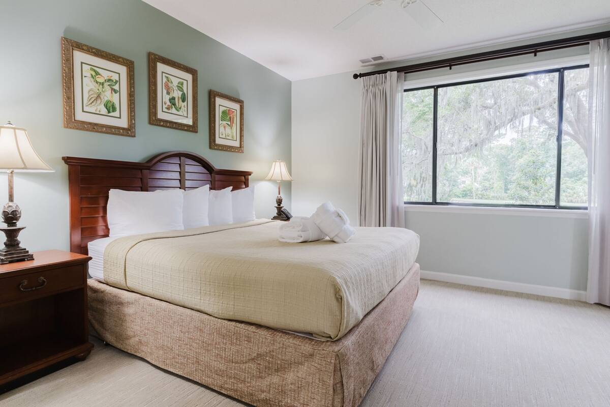 A hotel room with a large bed, two bedside tables with lamps, a wooden headboard, and three framed botanical prints on the wall.