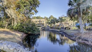 A riverside view with a bridge, trees, and a building with a patio area. - Spinnaker At Shipyard (Hilton Head Island)