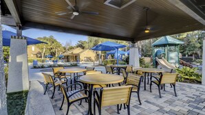 An outdoor patio area with round tables and chairs, umbrellas, and a playground in the background. - Spinnaker At Shipyard (Hilton Head Island)