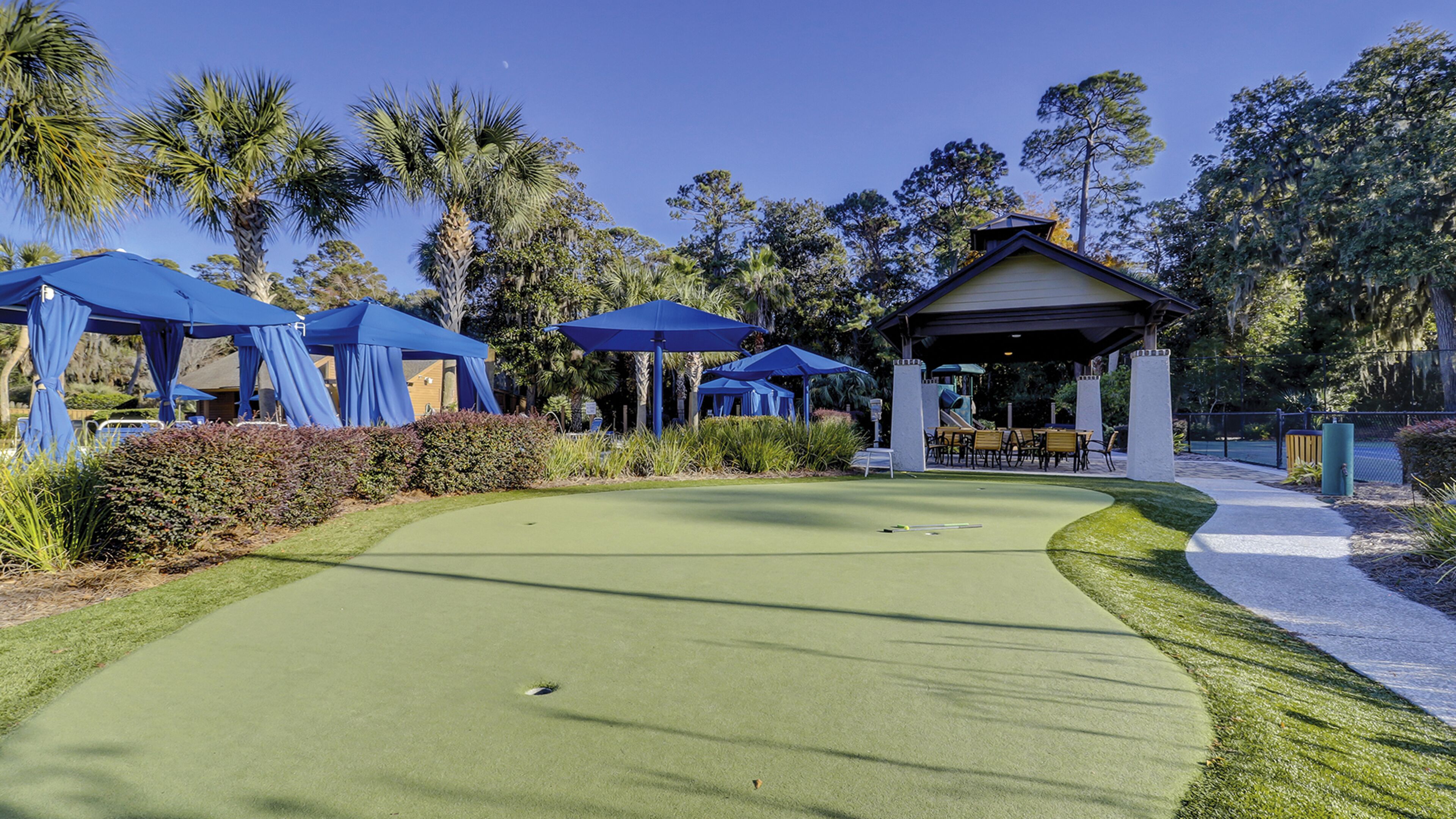 Ein Golfplatz mit Putting Green, blauen Sonnenschirmen und einem Pavillon.