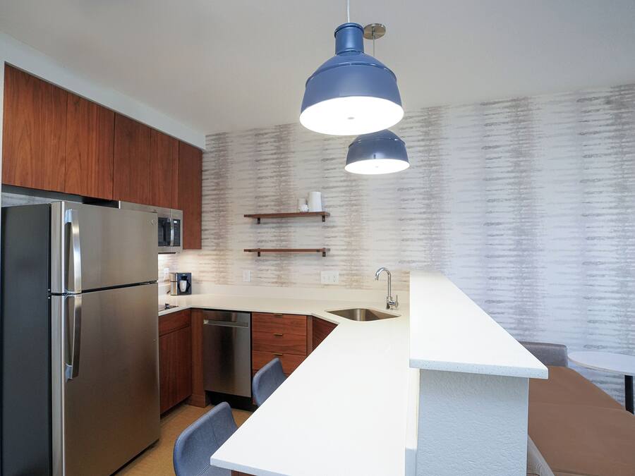 A modern kitchen with a stainless steel refrigerator, a microwave, a sink, and a bar area.