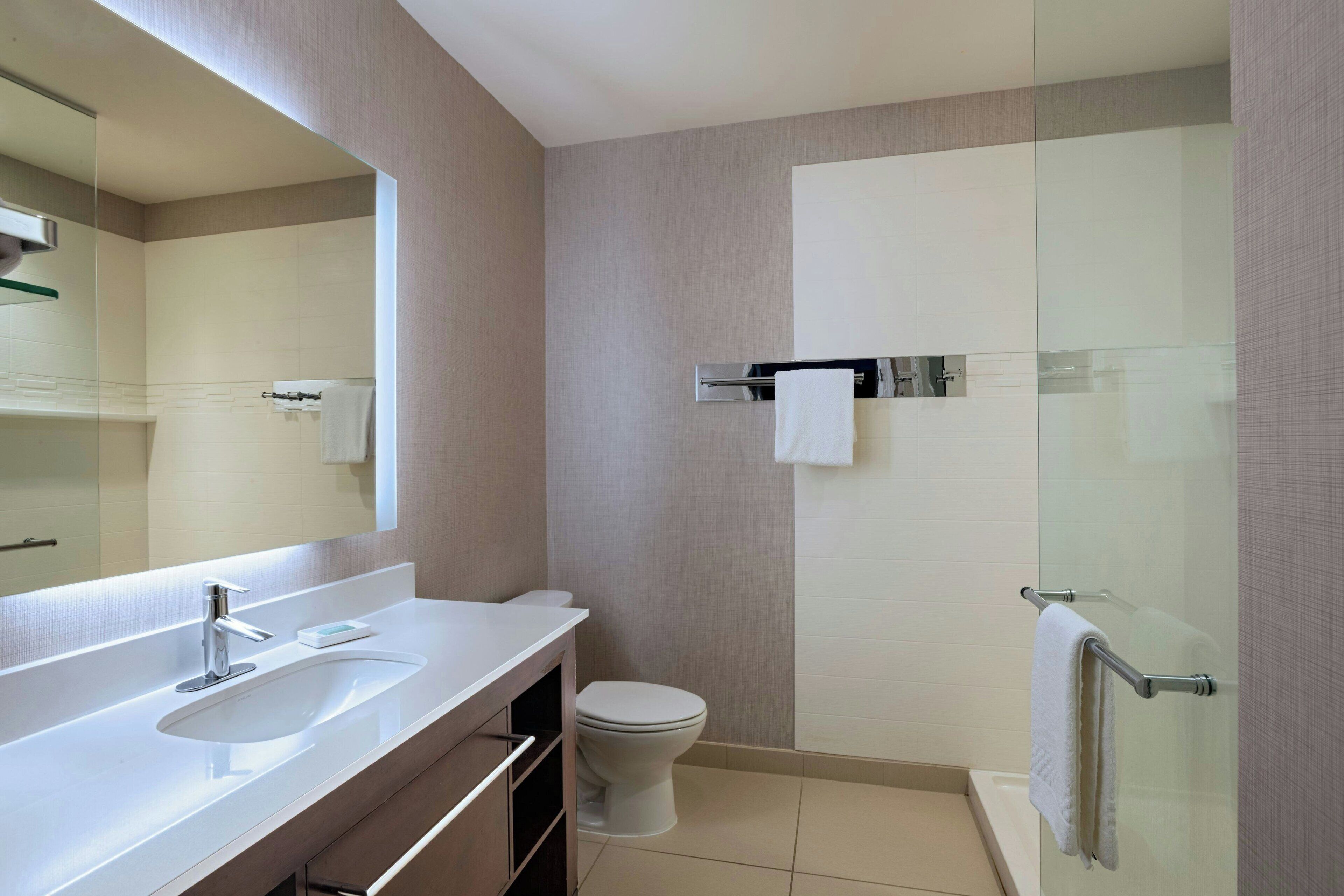 A modern bathroom with a large mirror, a sink, a toilet, and a glass shower enclosure.