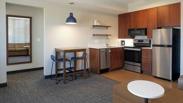 A compact kitchenette with a microwave, refrigerator, and stove. There is a small dining area with a table and chairs.