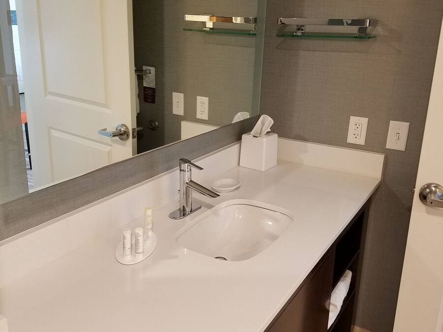 Un baño moderno con un lavabo blanco, un espejo grande y un estante de vidrio sobre el espejo.