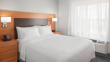 Habitación de hotel con una cama grande, dos mesitas de noche con lámparas, un teléfono sobre la mesa izquierda y una ventana con cortinas translúcidas.