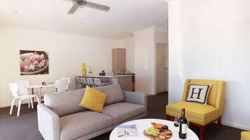 Una sala de estar moderna con un sofá gris, un sillón amarillo y una mesa de centro redonda con una revista, vino y aperitivos.