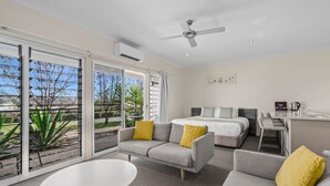 A modern hotel room with a large bed, a sofa, a dining table, and a balcony with a view of greenery. - H Boutique Hotel (Pokolbin)