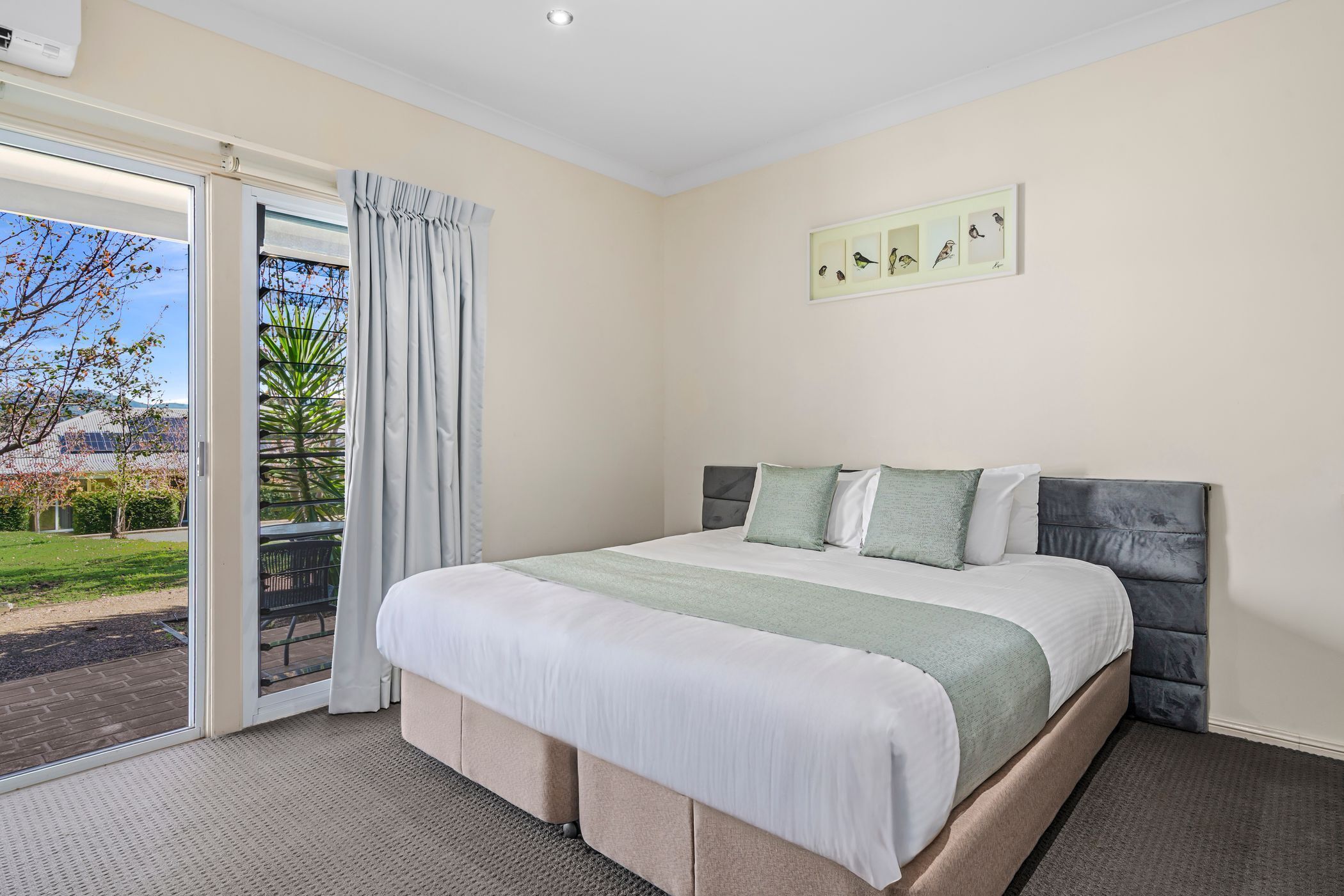 A bedroom with a large bed, a sliding glass door to a patio, and a framed picture on the wall.