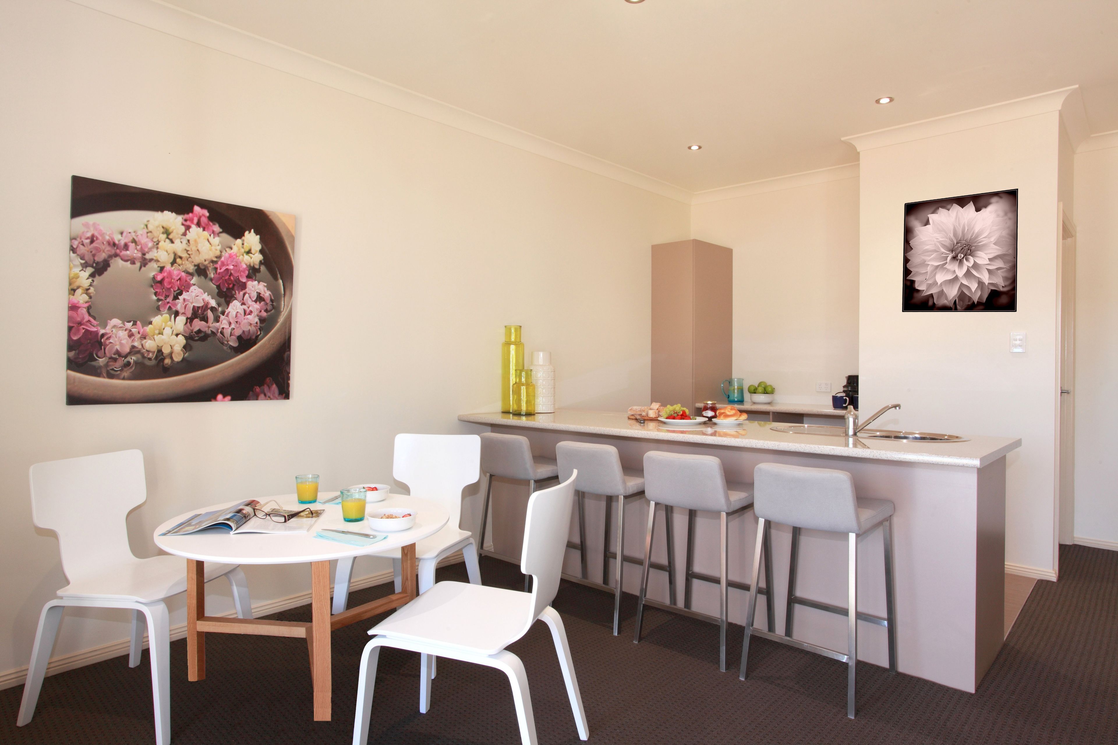 A modern kitchen with a central island, white bar stools, and a dining table with chairs.