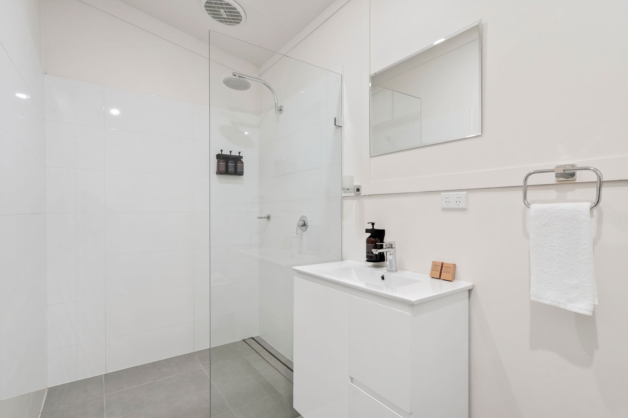A modern bathroom with a glass-enclosed shower, a white sink with a mirror above it, and a towel rack with a white towel.