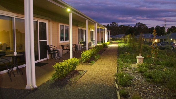 A motel with a covered patio area, outdoor seating, and a pathway leading to the entrance. - H Boutique Hotel (Pokolbin)