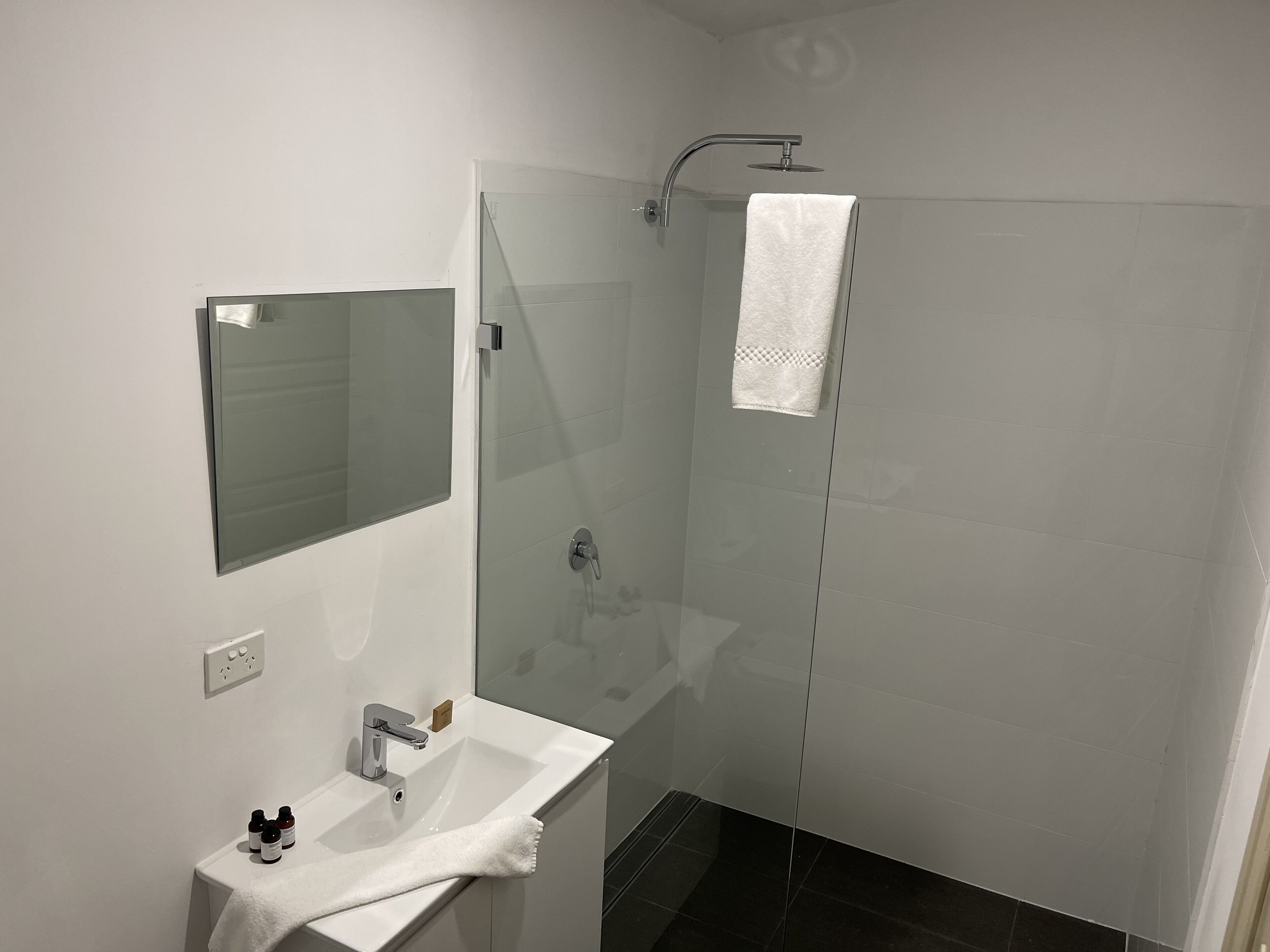 Ein modernes Badezimmer mit Duschkabine aus Glas, einem weißen Waschbecken und einem Spiegel.