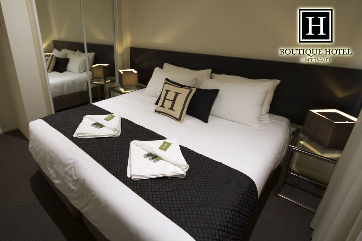 Ein Hotelzimmer mit einem großen Bett, zwei Nachttischen, einem Spiegel und einem Schild mit dem Hotelnamen und der Adresse.