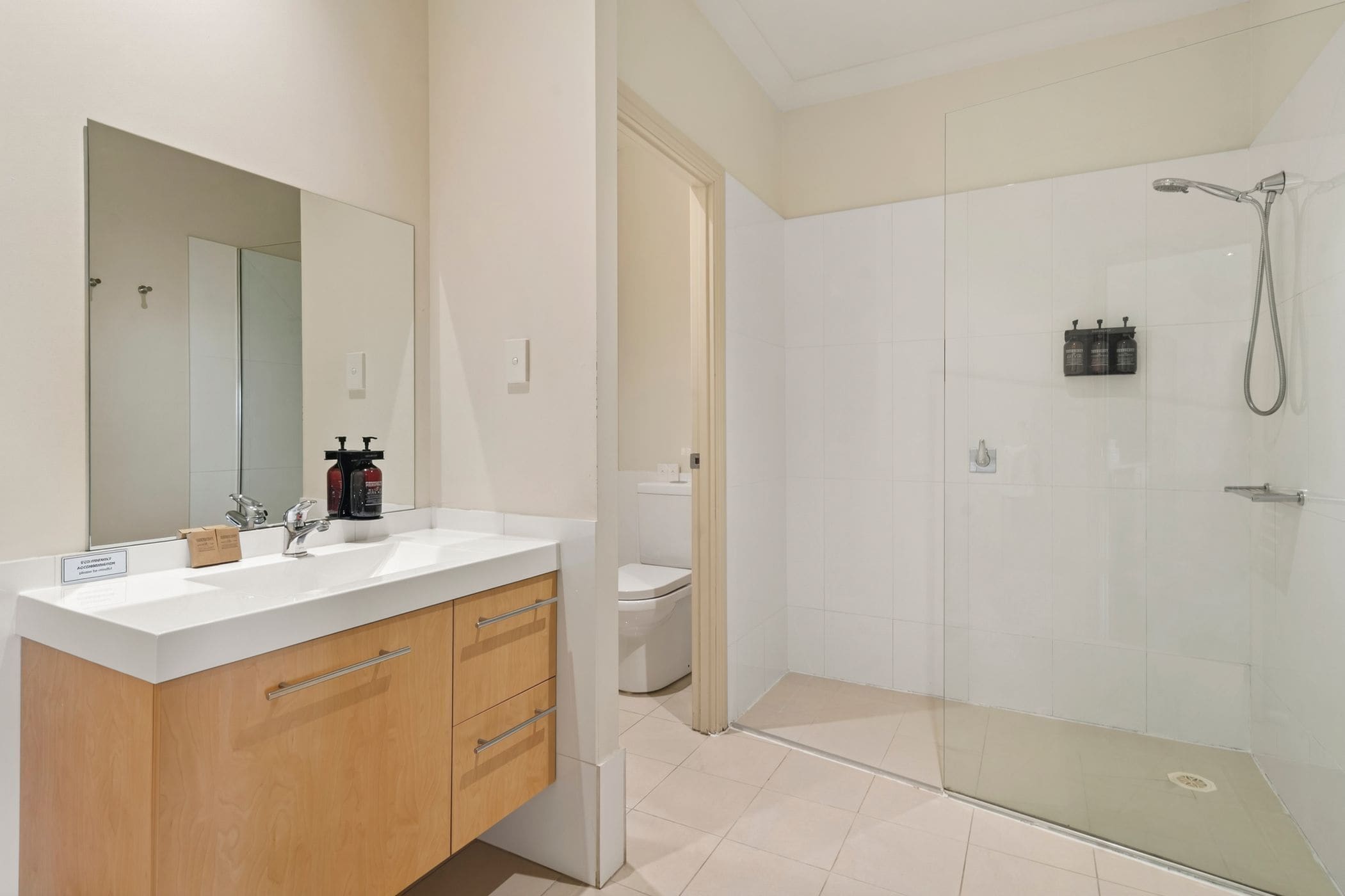 A modern bathroom with a glass-enclosed shower, a white sink with wooden cabinets, and a large mirror.
