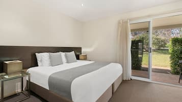 Une chambre d’hôtel avec un grand lit, une table en verre, une table de chevet et une vue sur un jardin, accessible par une porte-fenêtre coulissante.