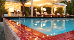 A swimming pool with tiled edges, lounge chairs, and a covered seating area with umbrellas. - Pousada Villa dos Graffitis (Cairu)