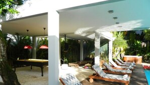 Un espace aménagé au bord de la piscine, avec des chaises longues, une table et un parasol rouge.