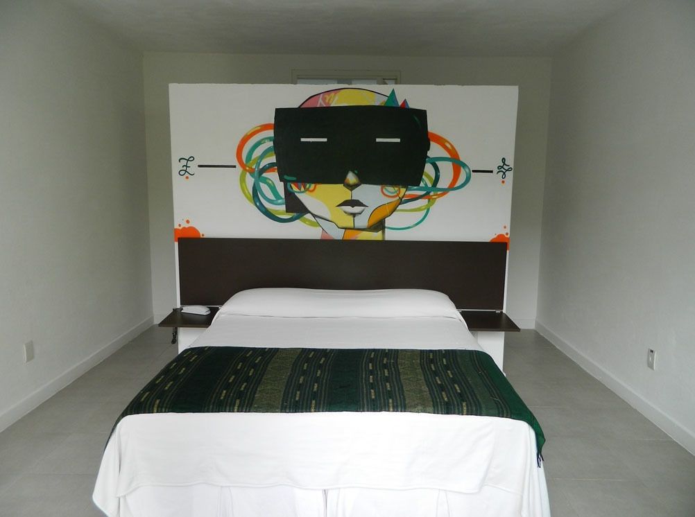 A bedroom with a bed, a nightstand, and a wall with a colorful abstract painting.