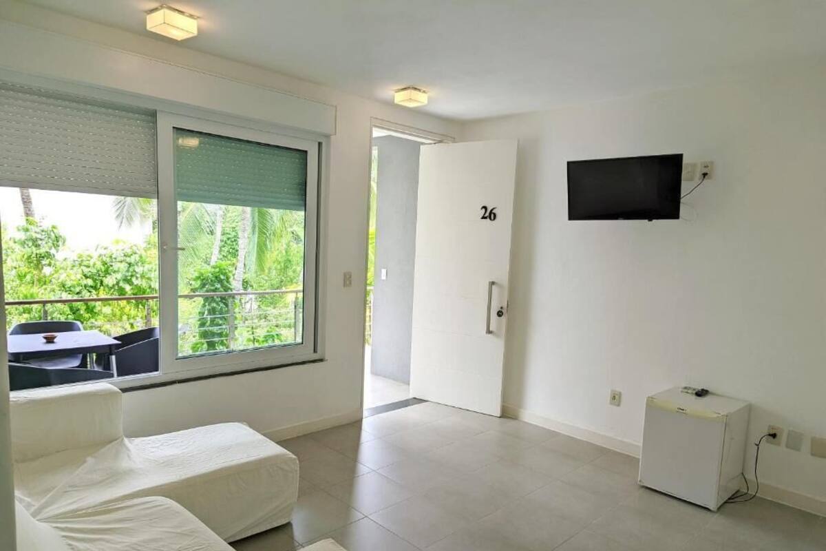 Quarto de hotel moderno com uma grande janela, uma televisão de tela plana na parede e um pequeno frigorífico.