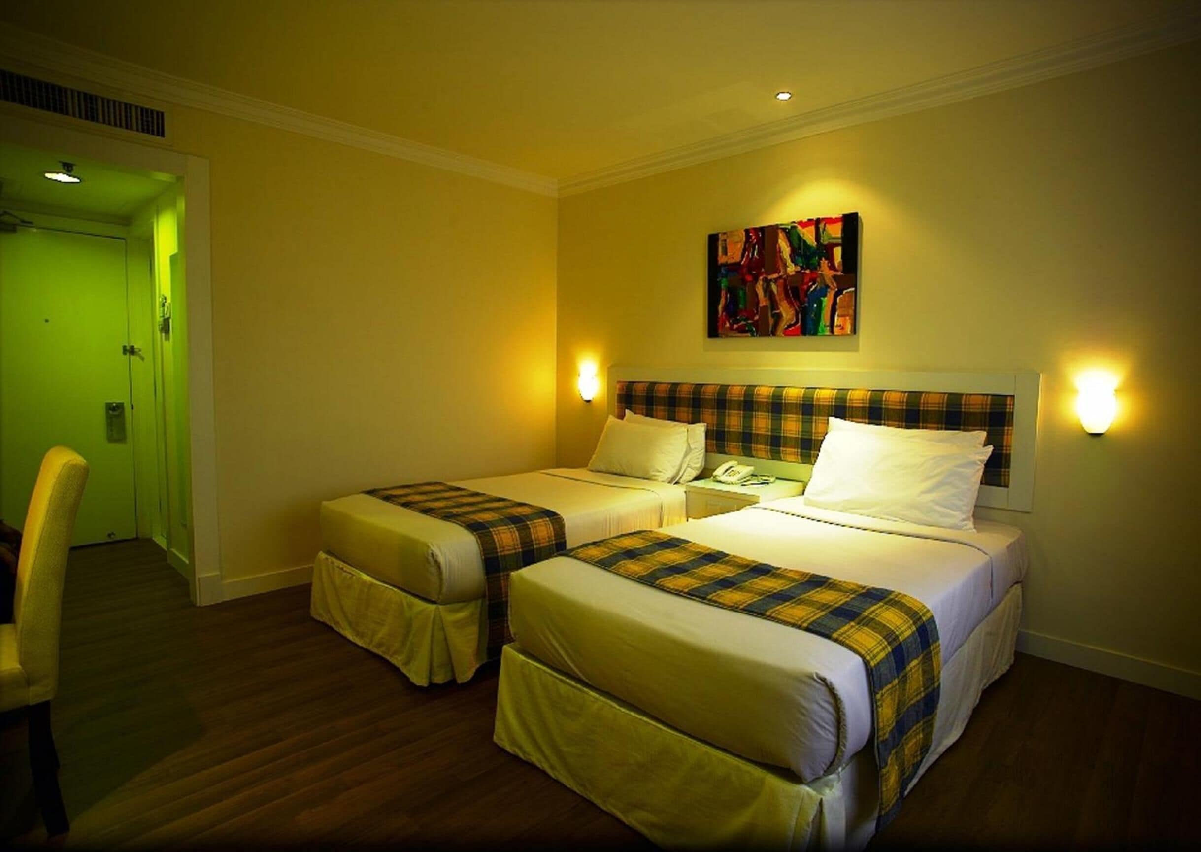 A hotel room with two beds, a painting on the wall, and a green door.