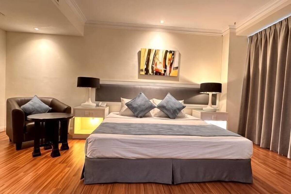A hotel room with a large bed, two bedside tables with lamps, a chair, and a painting on the wall.